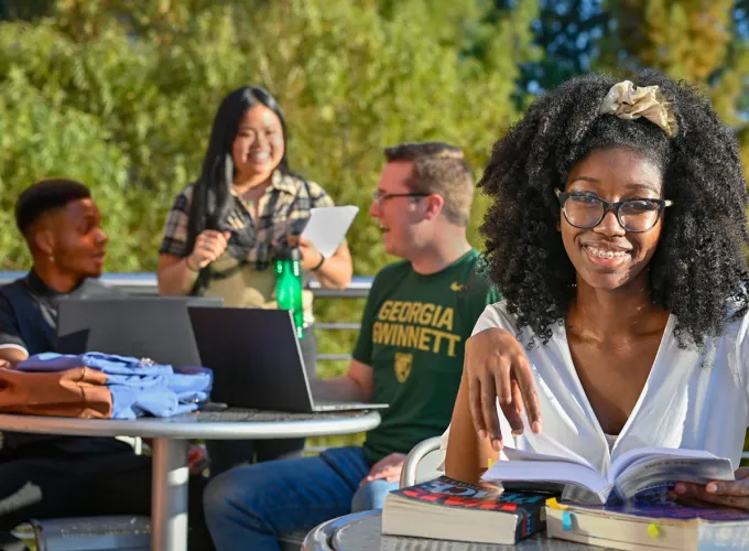 A female student smiling at the camera and three students behind her talking