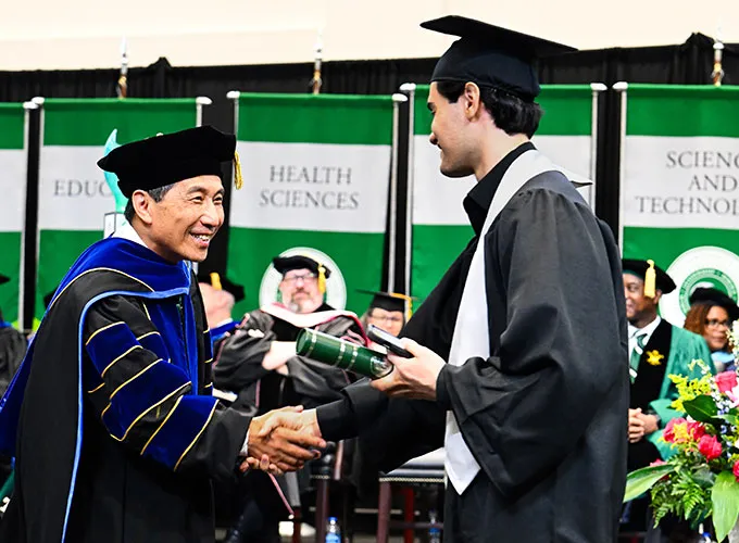 School of Business Dean Yu shaking hands with a business graduate during commencement