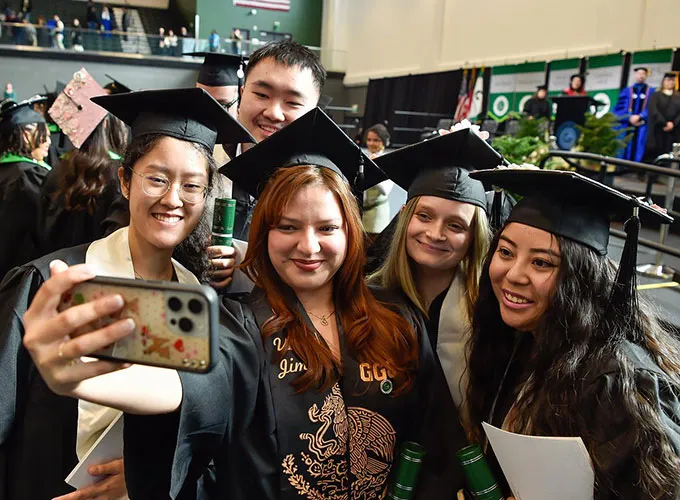 group of diverse grads taking a selfie at the end of commencement