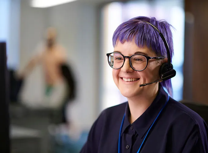 Purple-haired woman taking calls on a headset in an office