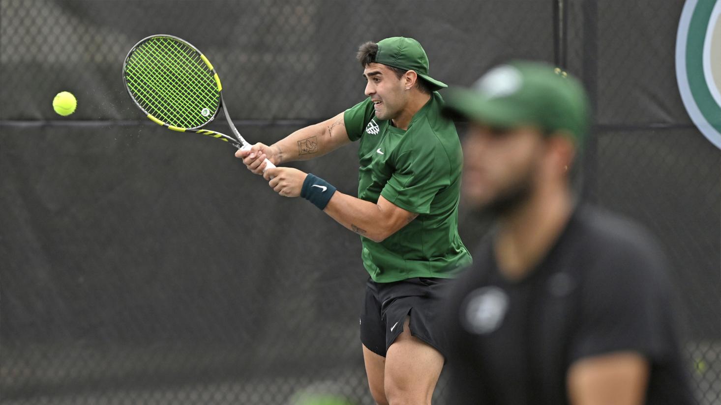 Male student swinging tennis racket.
