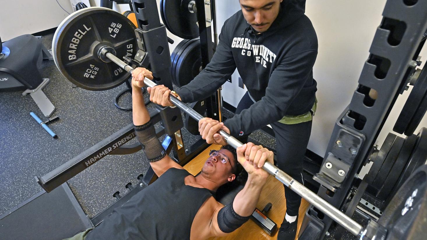 Male student helping other male student lift a barbell