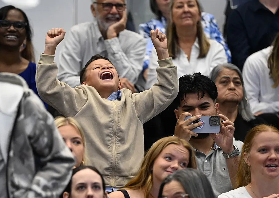 cheering boy with arms raised among family and friends celebrating grads