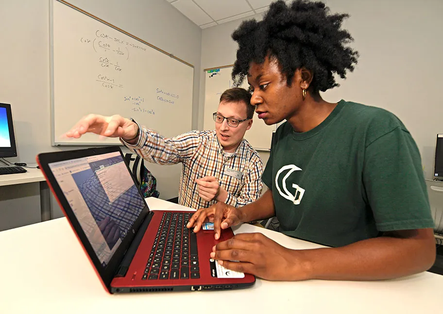 student using laptop with faculty member tutoring