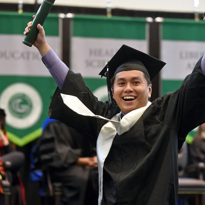 GGC grad on stage with hands raised in celebration