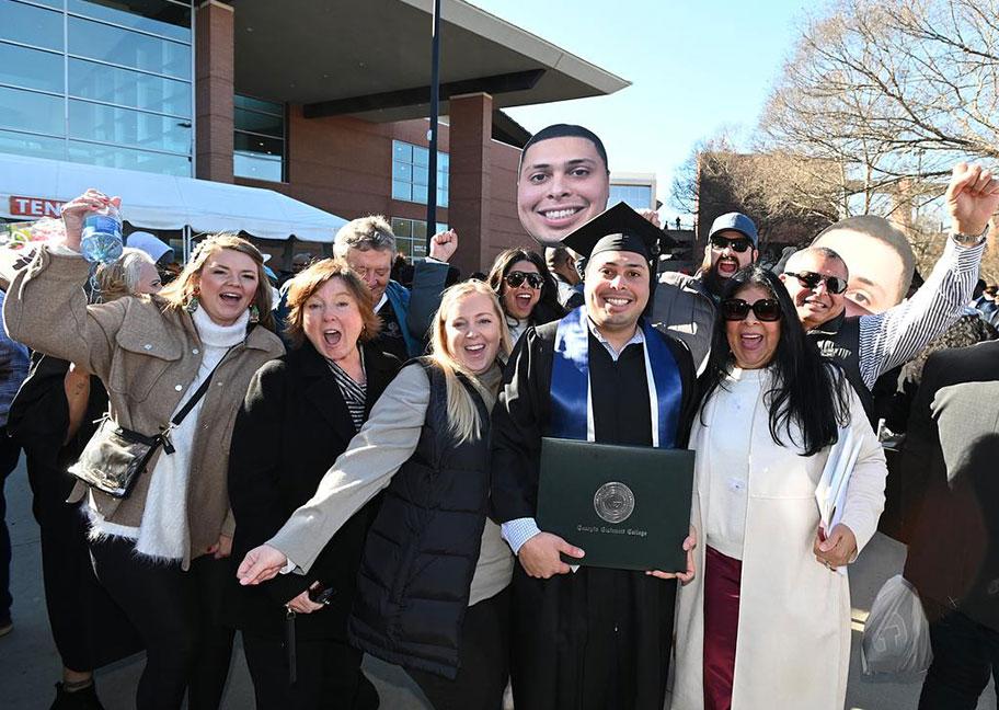 grad outside with family and friends cheering and holding up placards with grad's face