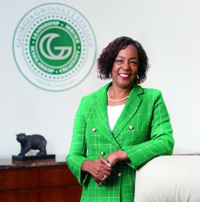 Dr. Jann L. Joseph leaning on a white chair with GGC seal and small grizzly statue behind her