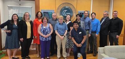 A group of 12 faculty members posing for a picture with the college president in an office