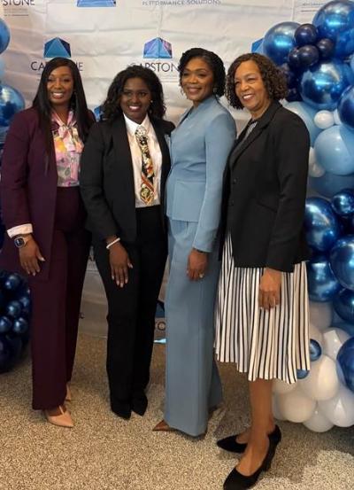 Four women posing for a picture in front of multicolor blue and white decorative balloons