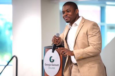 Benjamin Coker standing on stage at the podium holding a microphone in his hand at the 2026 Elite Scholars Summit