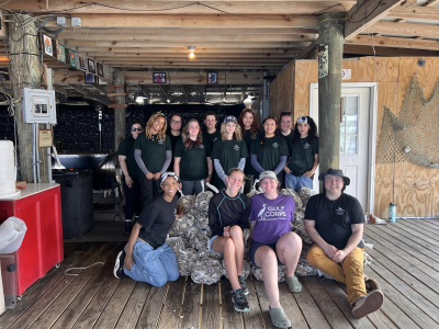 Group of GGC students posing atop a sack of oysters at Bama Bay Oyster Farm during 2026 Alternative Spring Break
