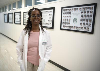 Dr. Paula Gordon posing for a photo in a white hall with picture frames along the wall